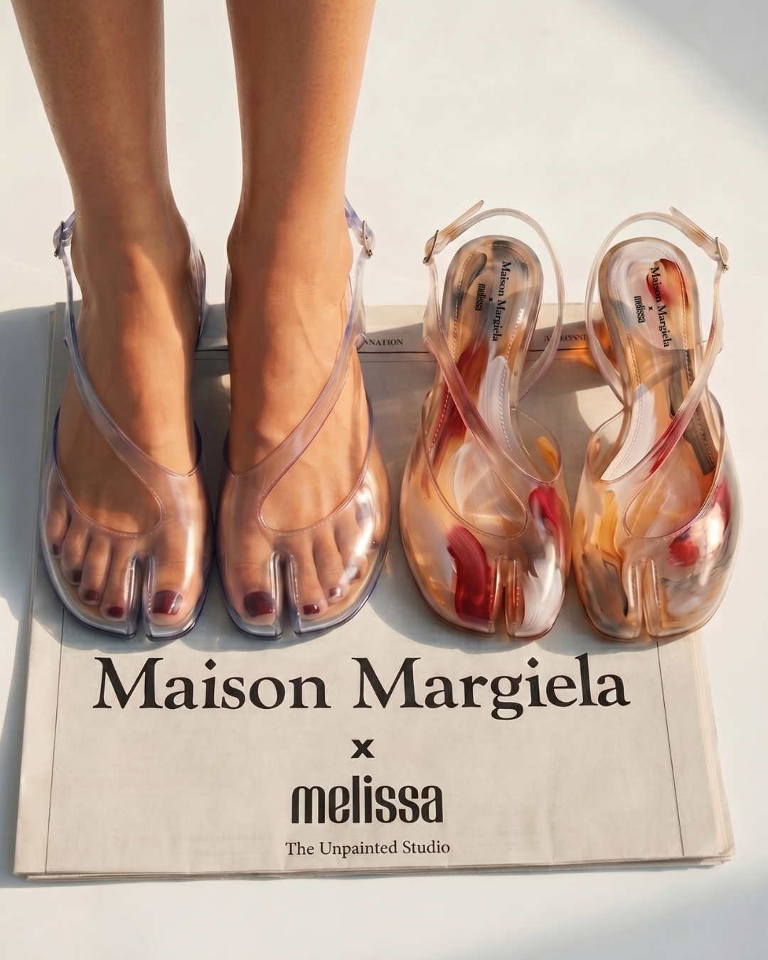 Editorial campaign image for Maison Margiela x melissa: split-toe jelly sandals, one pair worn and one hand-painted, photographed on printed newsprint